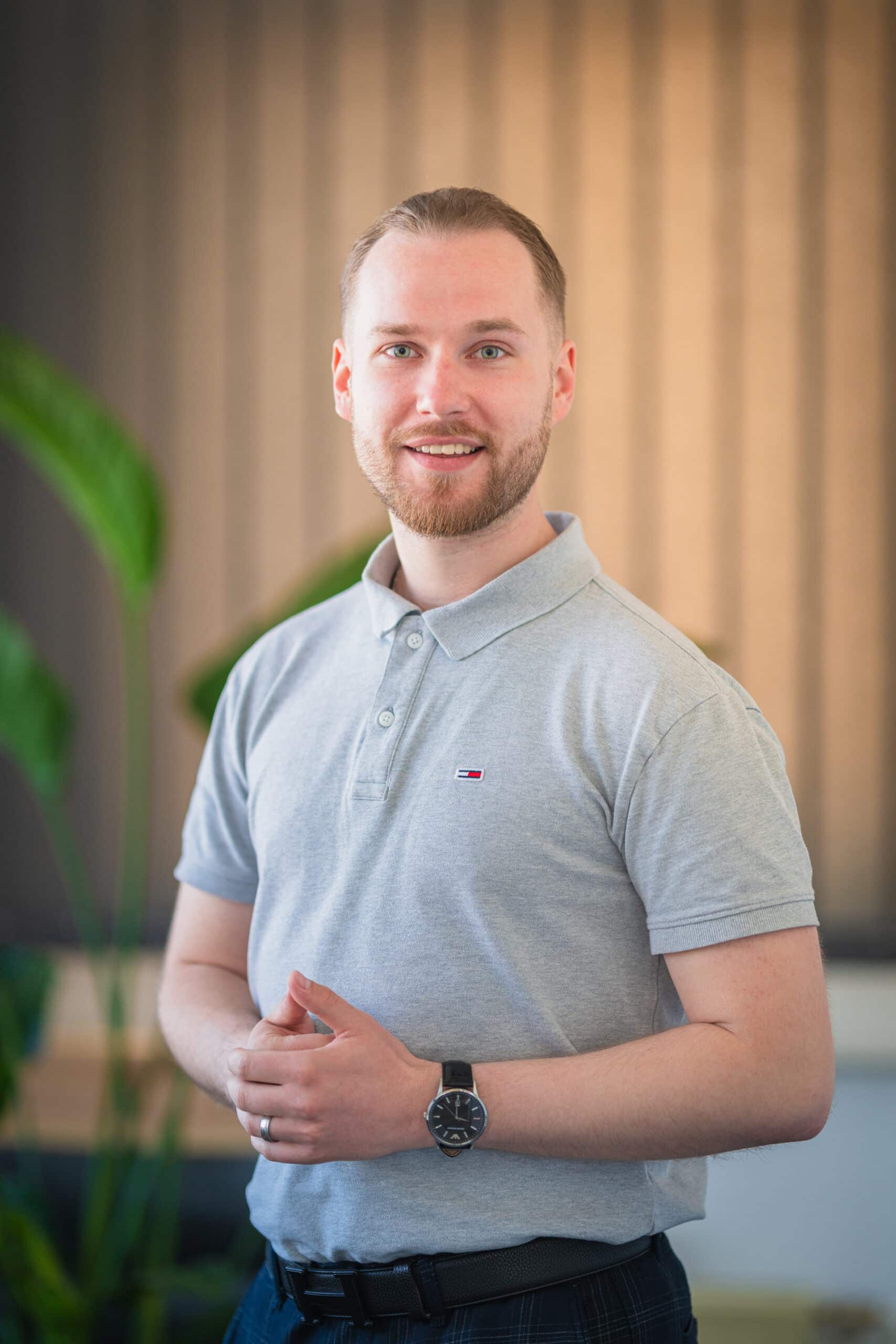 Mann im grauen Poloshirt steht lächelnd vor Pflanze.